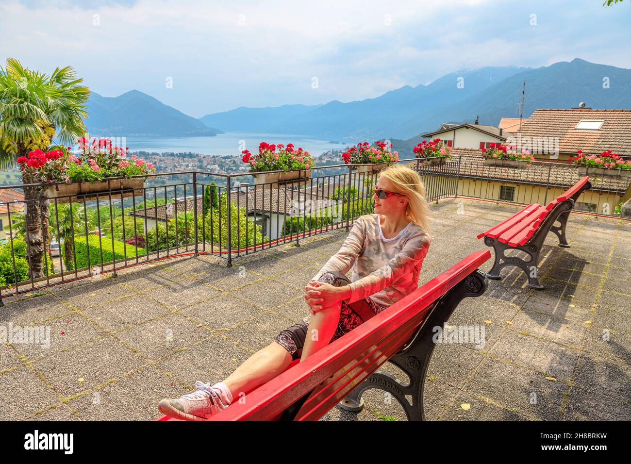 Woman sitting on top of Lake Maggiore in Switzerland. Swiss bench at aerial view lookout from Orselina town of Locarno and Ascona on Cardada mount Stock Photo