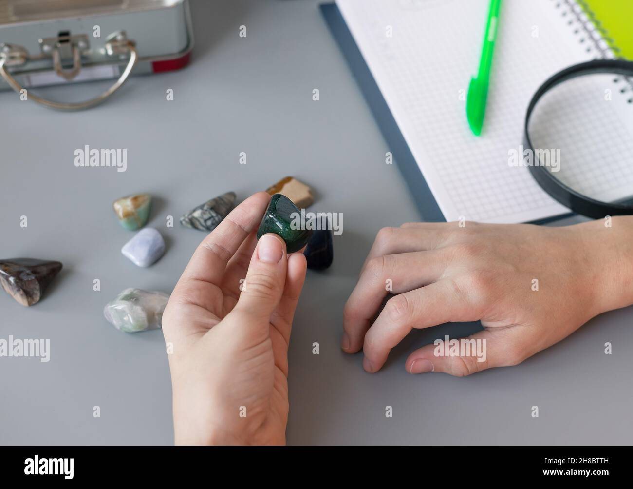 kids hands studying semiprecious stones on gray desk with supplies Stock Photo