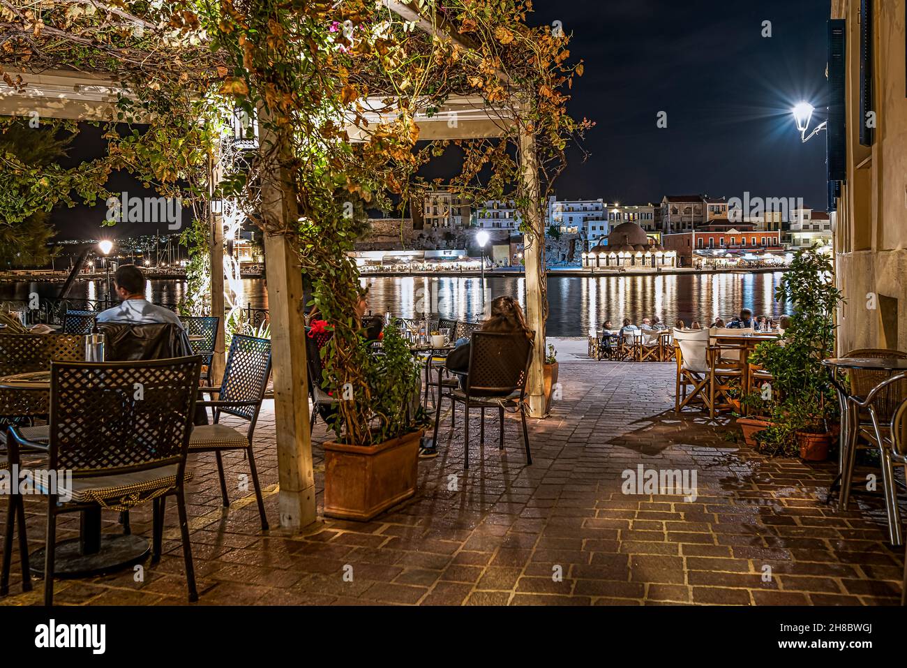 an outdoor restaurant at night with guests sitting in a pergola, looking out over the port of Chania, Crete, Greece, October 13, 2021 Stock Photo