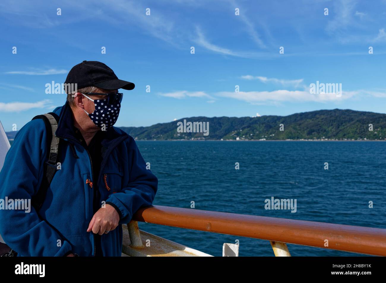 A man looks out from the deck of a ferry, he is wearing a mask as a prevention measure against Covid 19 Stock Photo