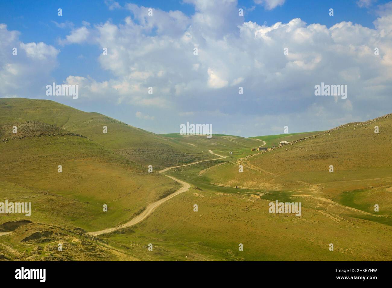 Country road winding between hills of valley. Village houses and small figures of residents are visible near hill on right side. Shot in Qashqadaryo r Stock Photo