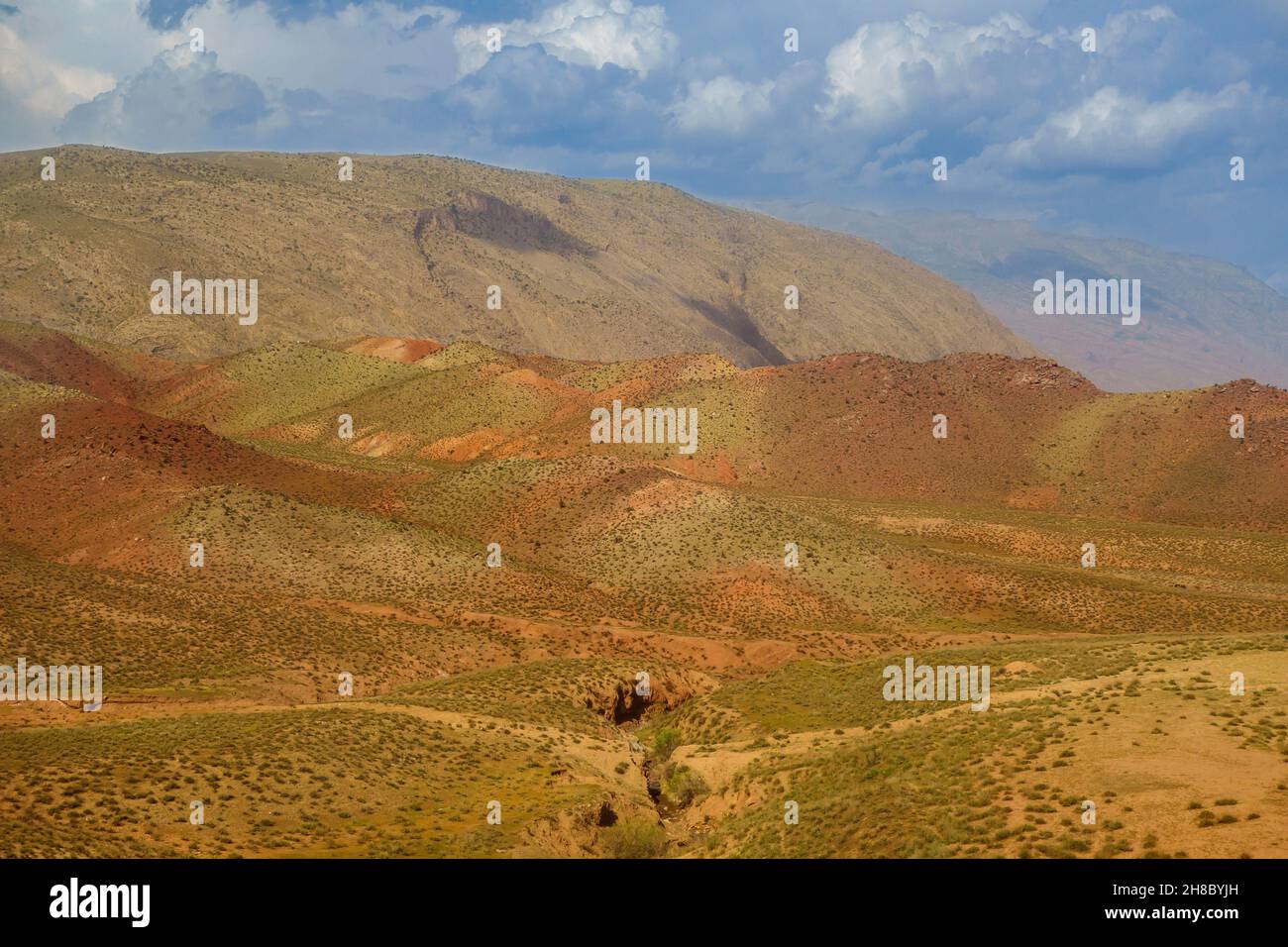 Colorful carpet of hills at foot of mountains against backdrop of scenic sky with clouds. Shot in Surkhandarya region in south of Uzbekistan near moun Stock Photo