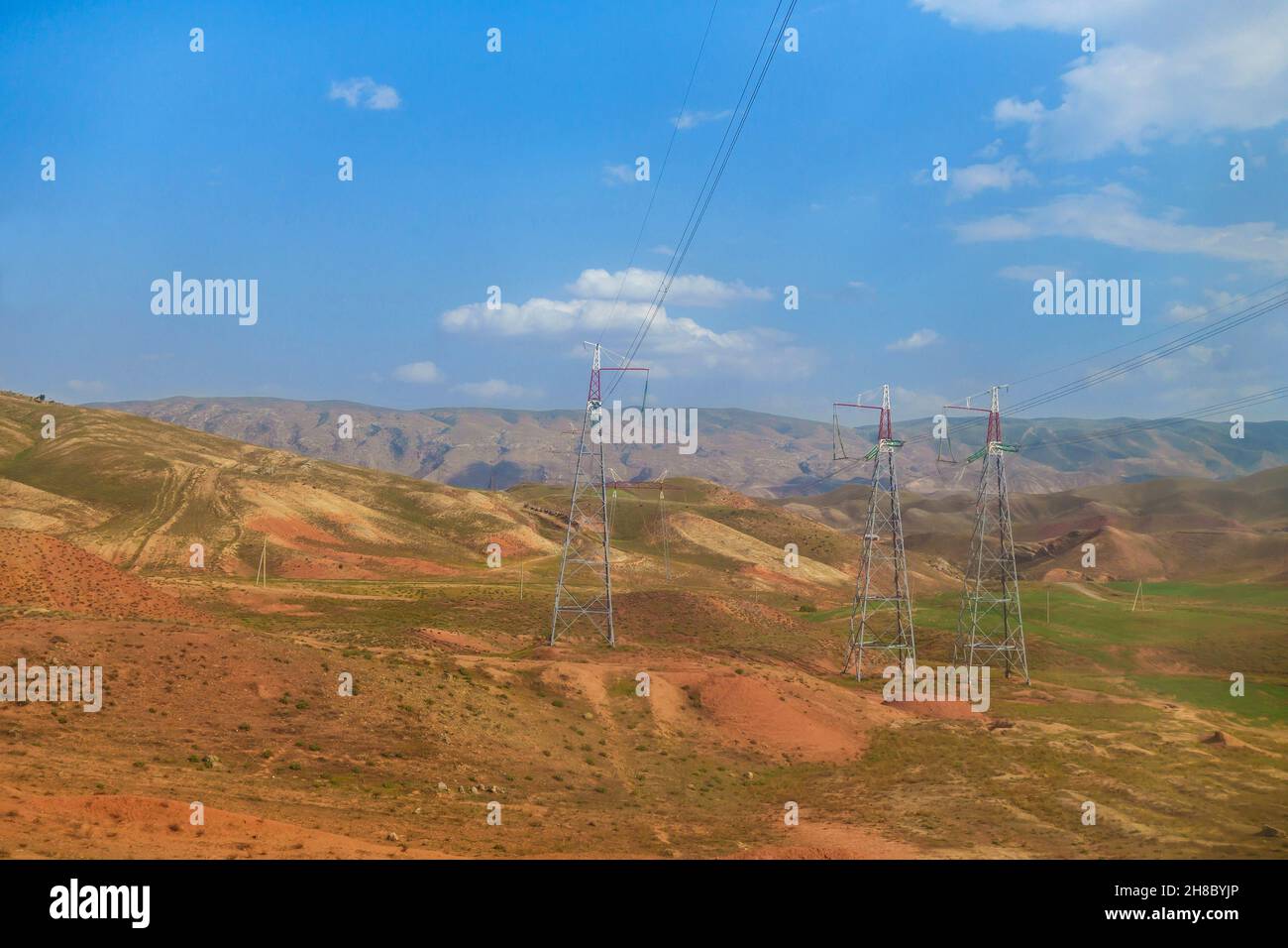 Power transmission towers in middle of colorful hills. Mountain range is visible in distance. Shot in Surkhandarya region in Uzbekistan near mountains Stock Photo