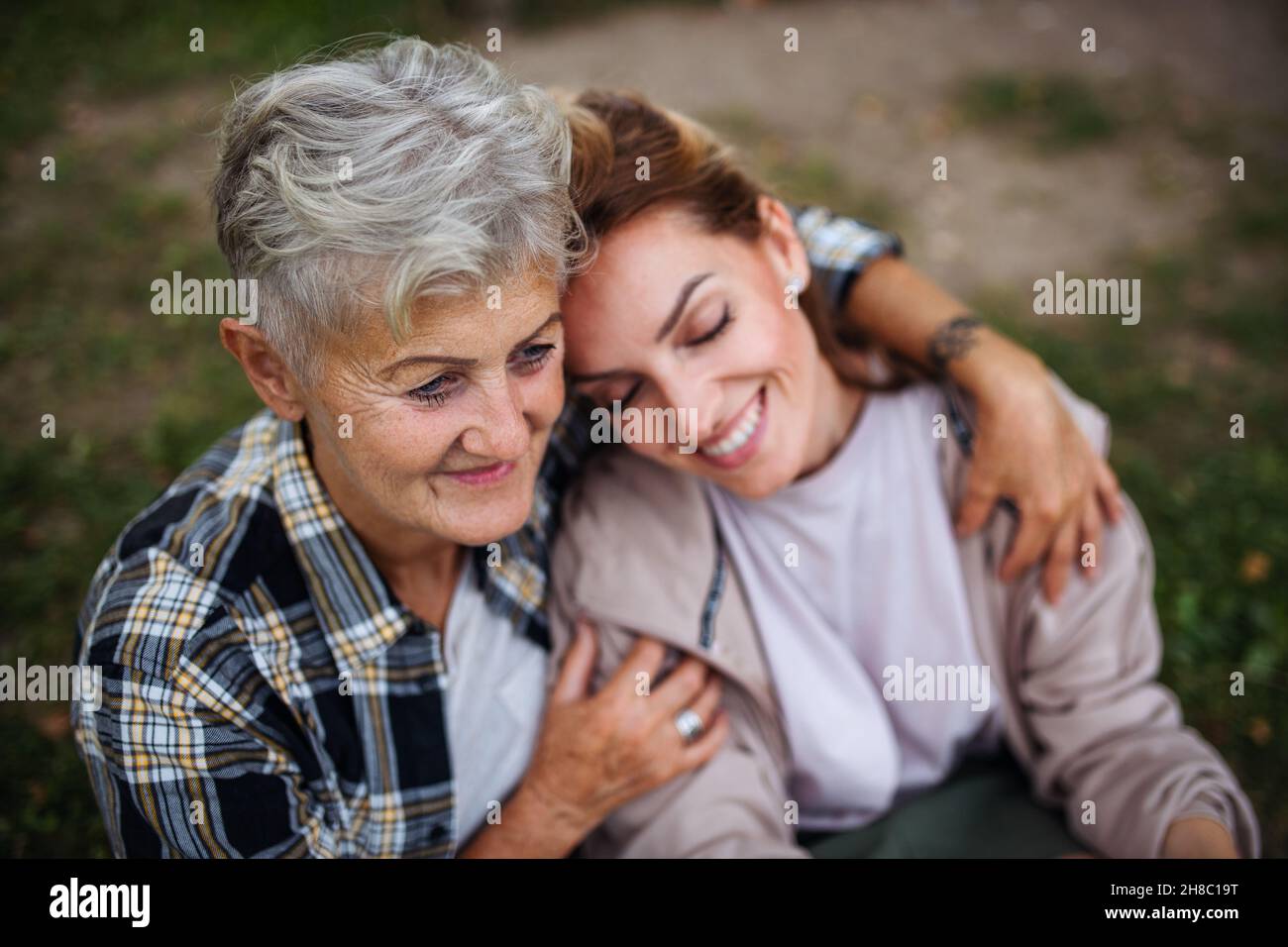 Close up of senior mother sitting on grass with adult daughter leaning