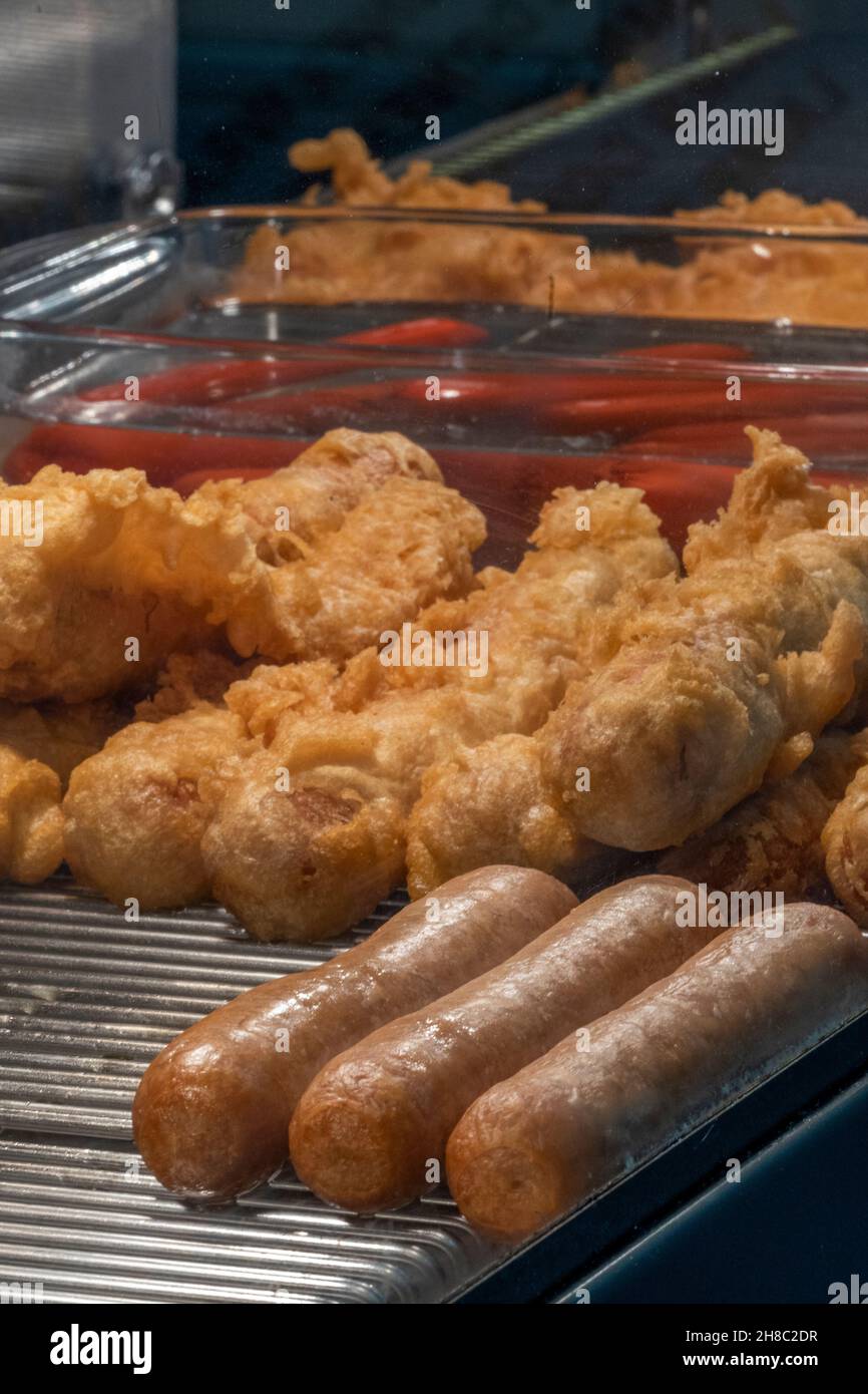 battered sausages and plain sausages with saveloy in heated display counter in fish and chip shop, fast food in a fryer at a takeaway food restaurant. Stock Photo
