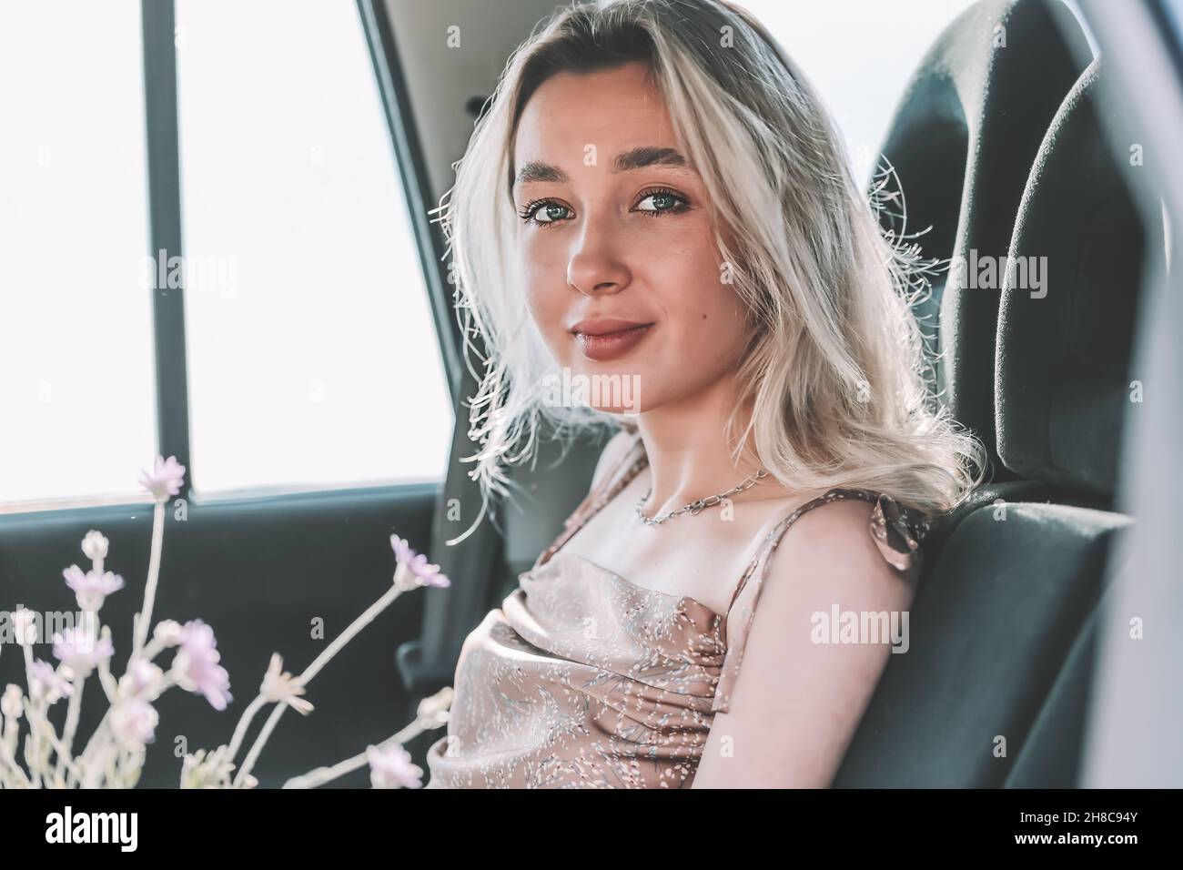 Young blonde girl sitting in the back seat of the car with flowers in defocus Stock Photo