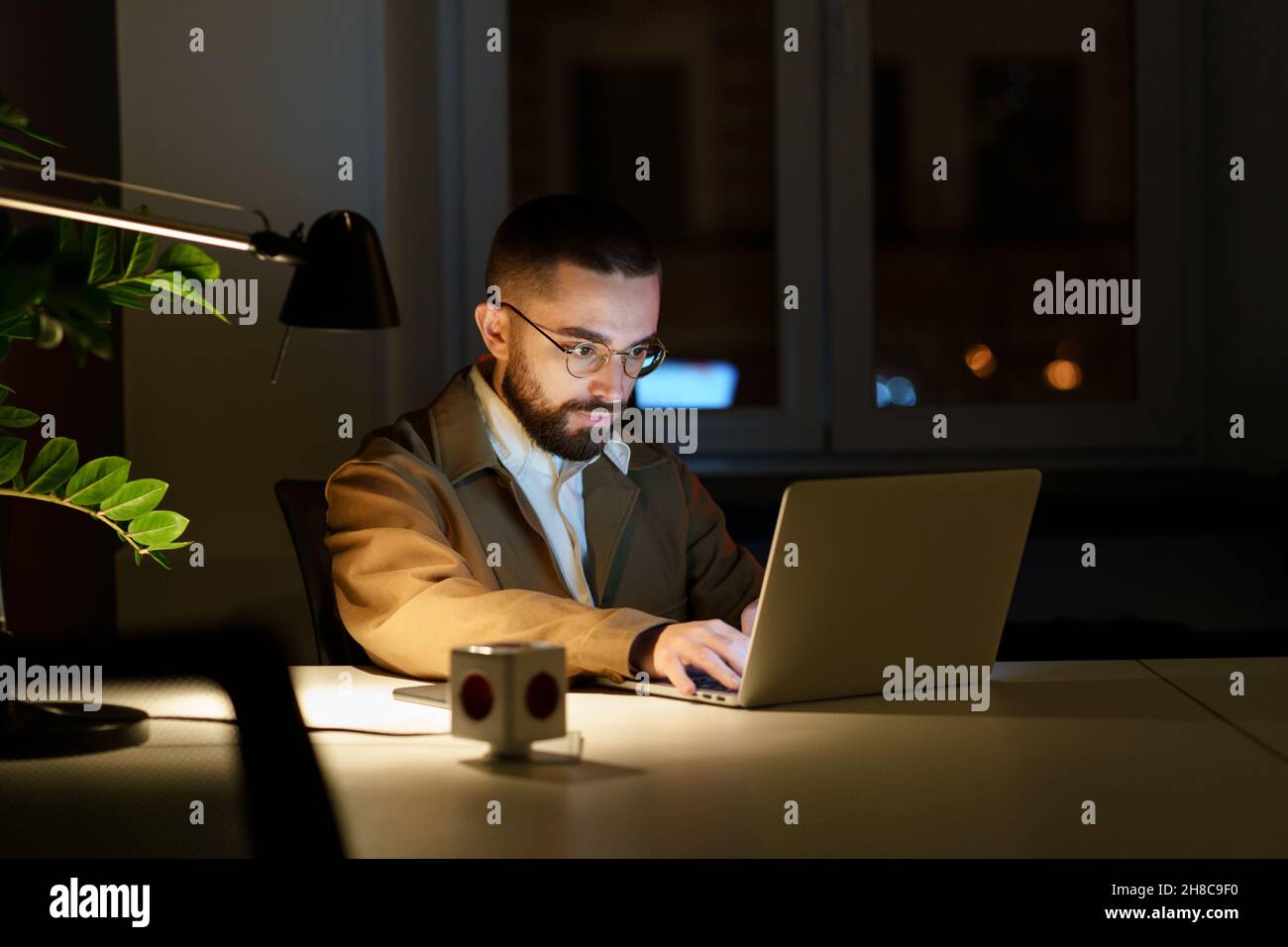 Concentrated programmer man work on laptop in evening in empty office o fixing bug in application Stock Photo