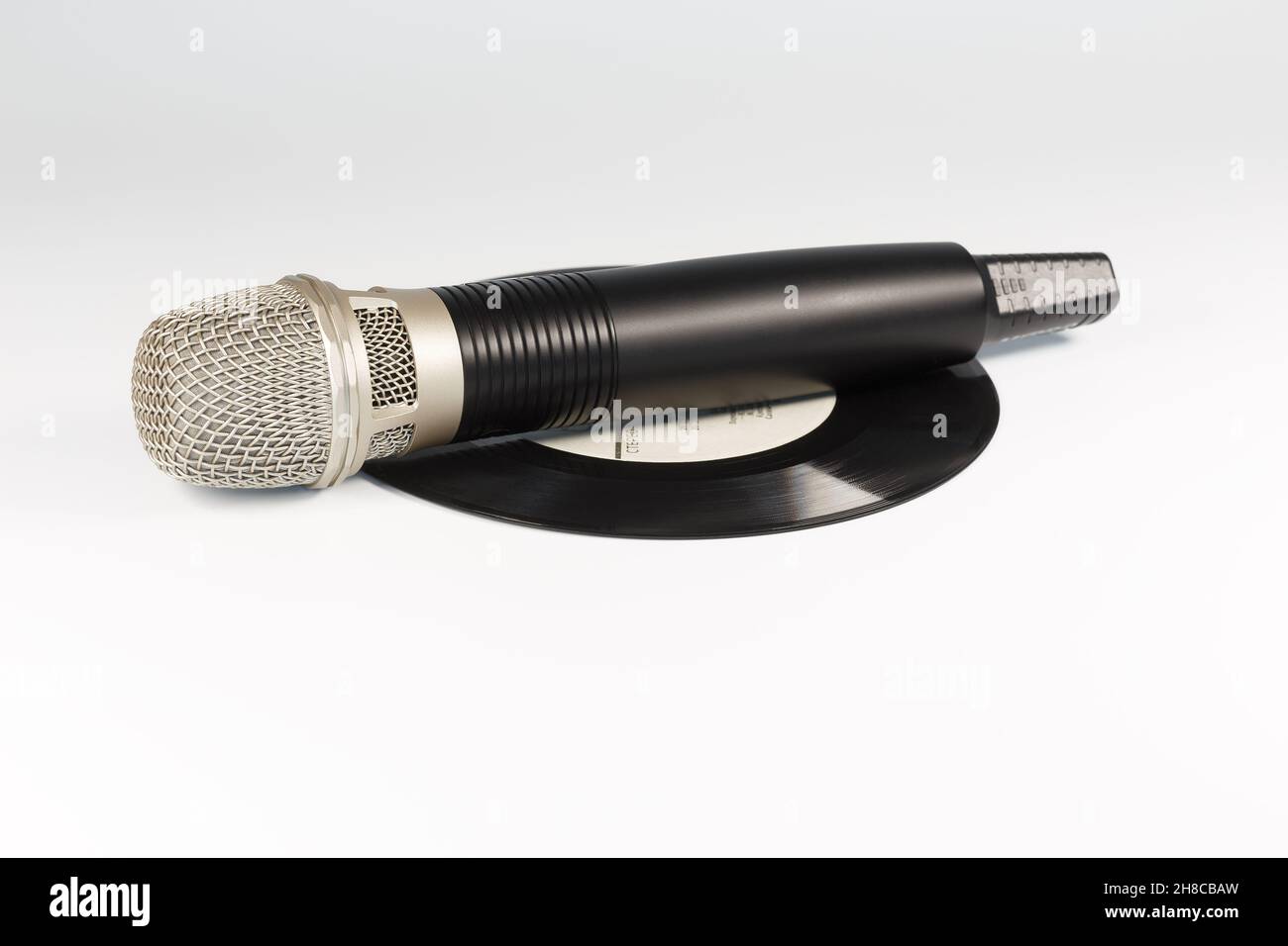 The microphone lies on a vinyl record, on a white background. Stock Photo