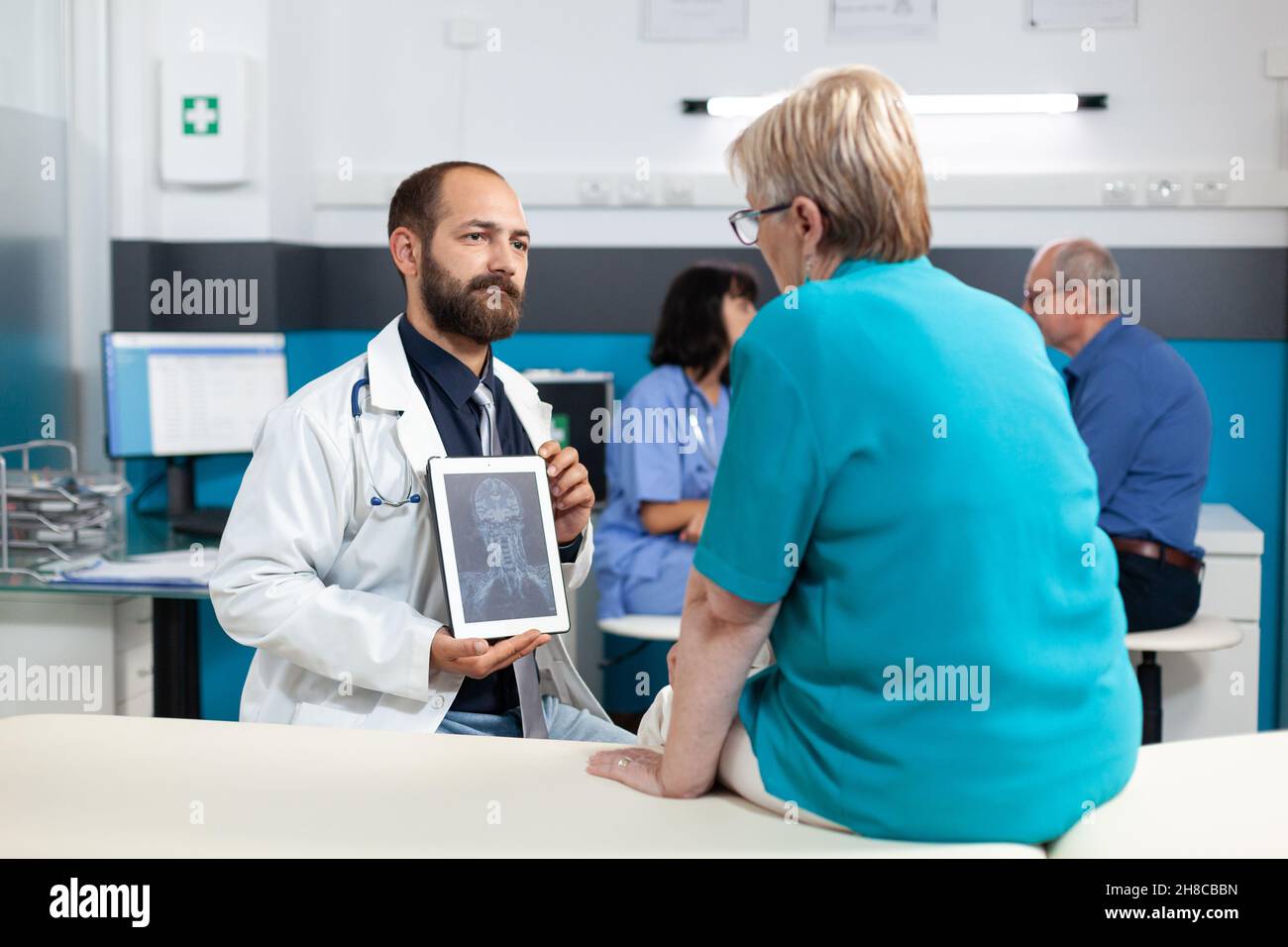 Doctor holding tablet with radiography for osteopathy diagnosis in medical office. Senior patient looking at x ray scan on gadget display for orthopedic analysis and rehabilitation. Stock Photo