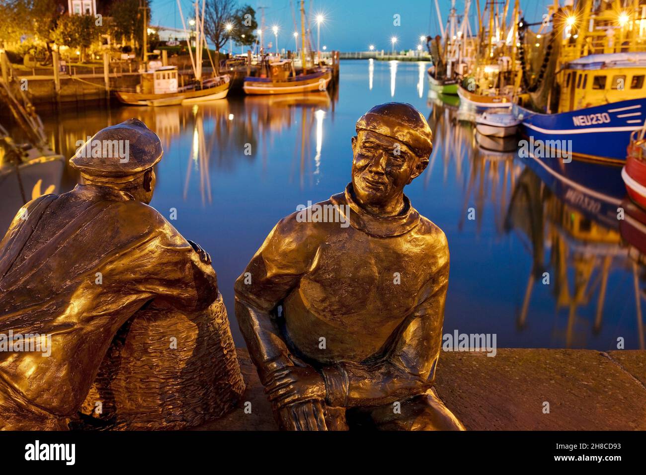 fishing harbour with shrimpers and sculpture Skulptur Alt- und Jungfischer in the evening, Germany, Lower Saxony, Neuharlingersiel Stock Photo