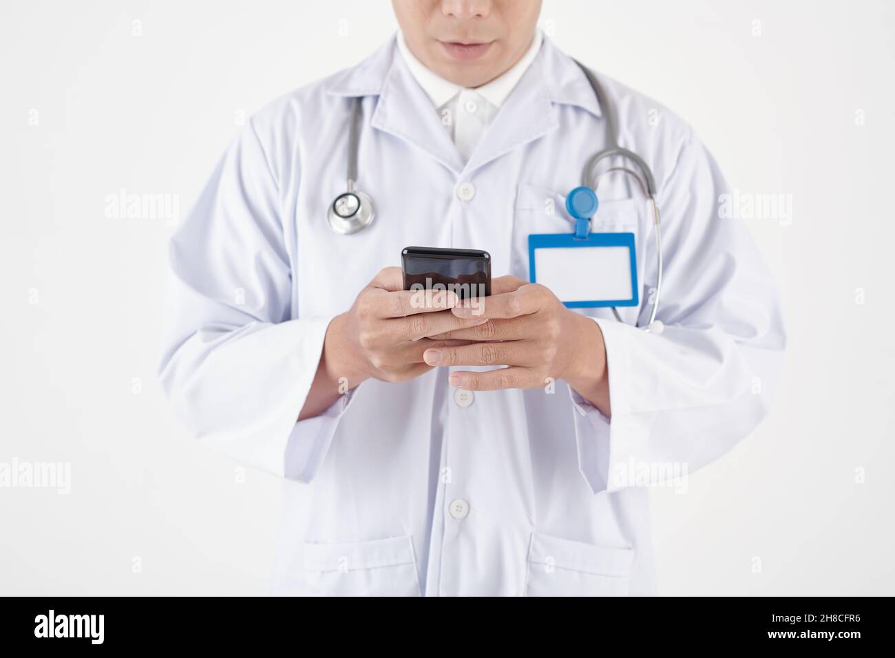 Serious general practitioner reading text messages on smartphone from patient or colleague Stock Photo