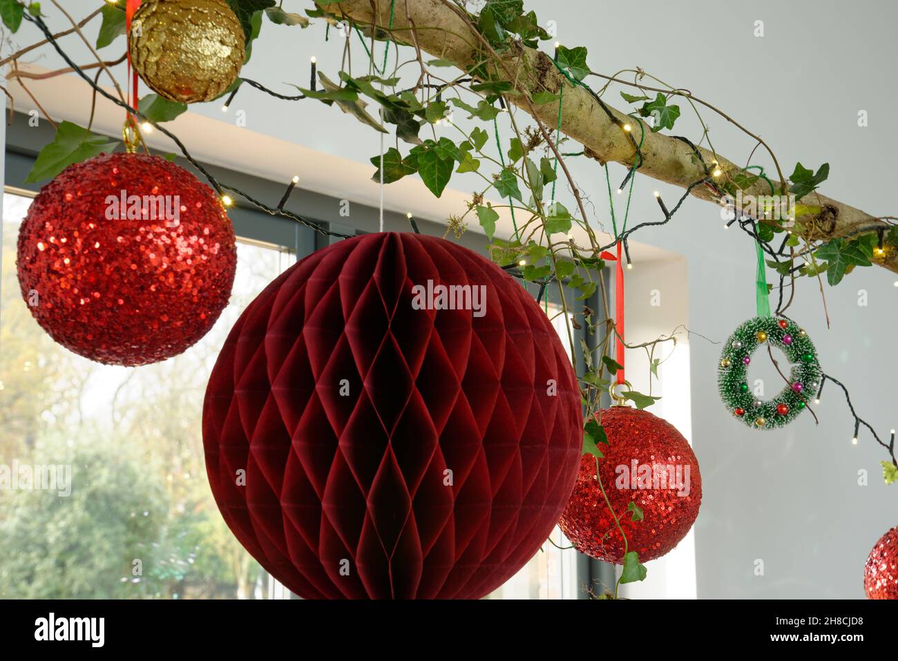 Christmas sphere decorations hanging from a wooden branch decorated with ivy and fairy lights