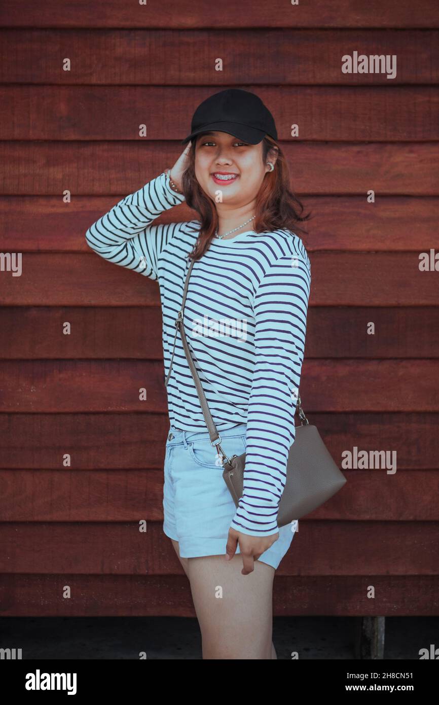 asian younger woman toothy smiling standing against wooden wall Stock Photo
