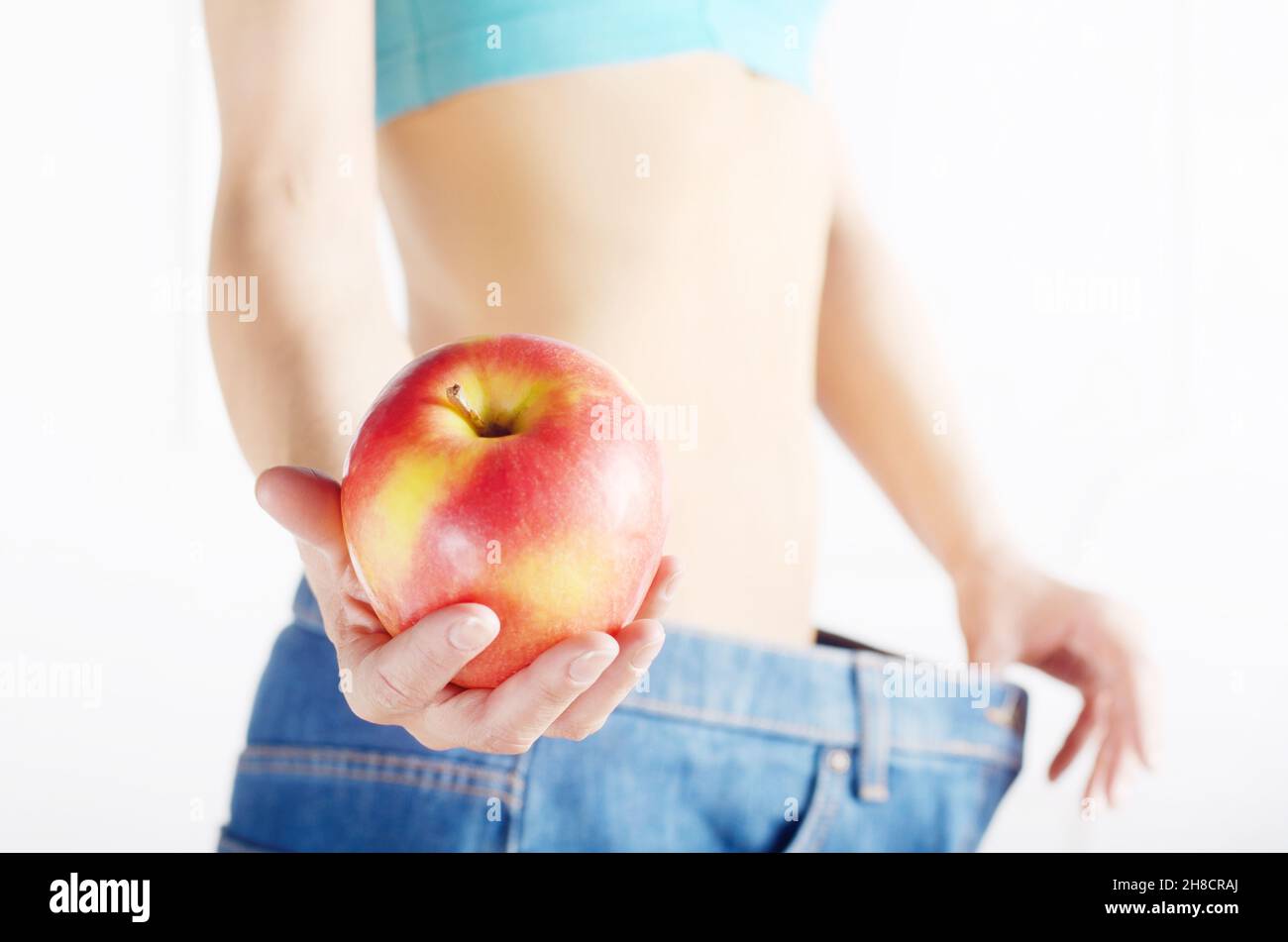 Caucasian female model in blue jeans with red apple showing her flat stomach. Healthy lifestyle and Weightloss concept. Stock Photo