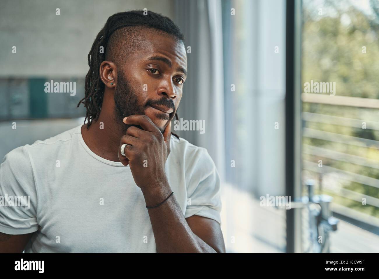Man touching his beard with one hand before mirror Stock Photo