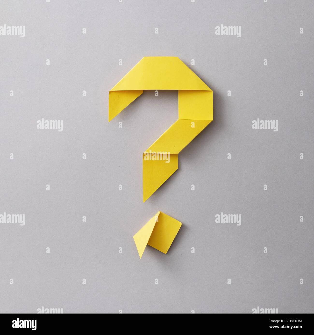 Origami question mark of neatly folded yellow paper on a square grey