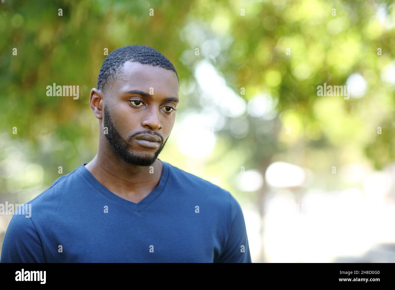 Worried man with black skin distracted looking away walking in a park Stock Photo