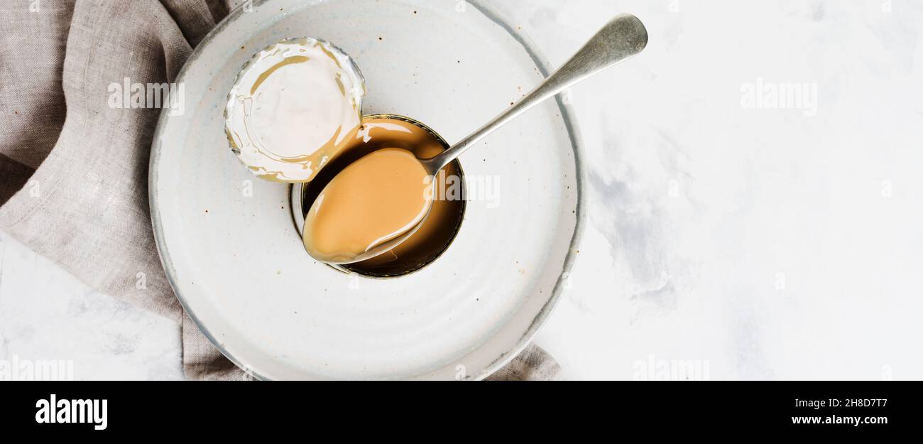 Condensed or evaporated milk in open tin on light concrete table. Top view. Stock Photo