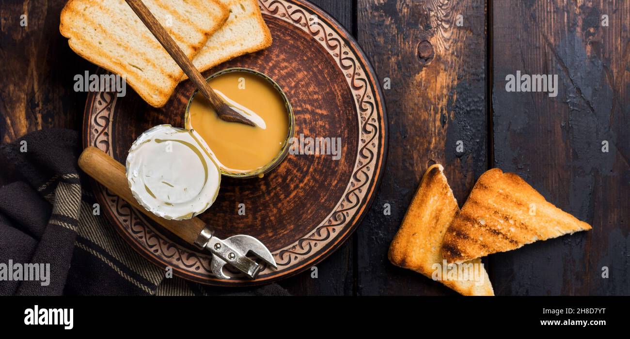 Condensed or evaporated milk in open tin on dark old wooden table. Rustic style.Top view. Stock Photo