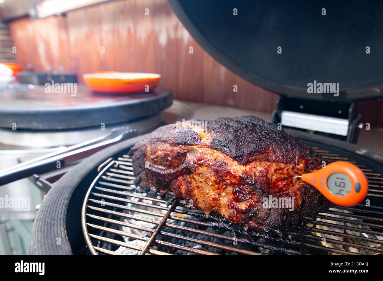 Outdoor kitchen smoker and flat top grill cooking a pork butt or shoulder using a meat thermometer to check internal temperature Stock Photo