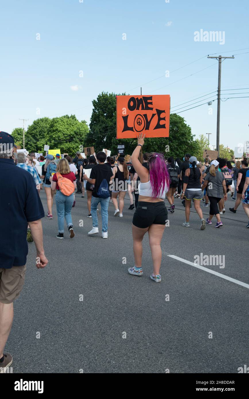 A woman with purple hair holds up a 'One Love' sign while walking in the BLM protest march in  Sterling Heights, Michigan on June 6, 2020. Stock Photo