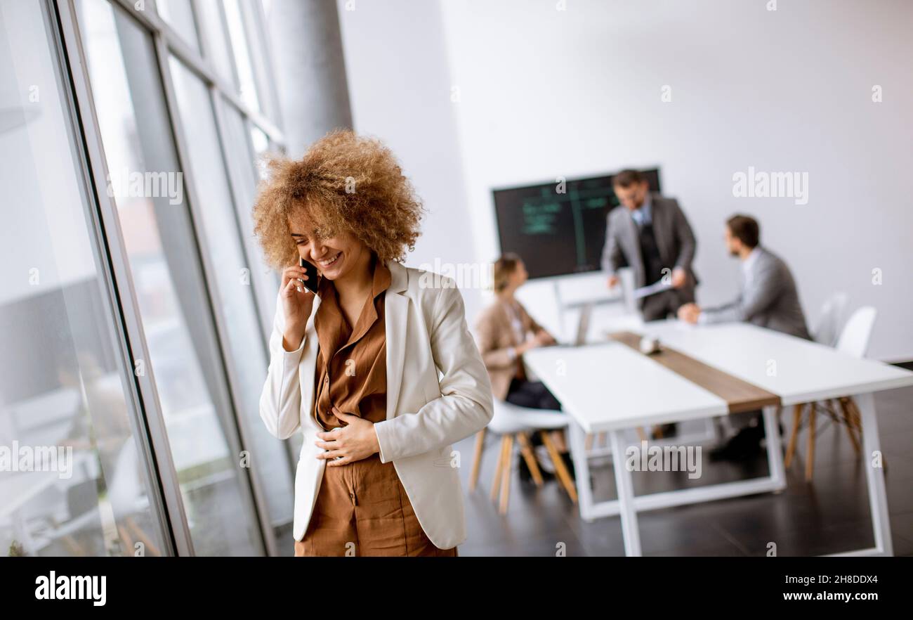Young curly hair businesswoman using mobile phone in the office with young people works behind her Stock Photo