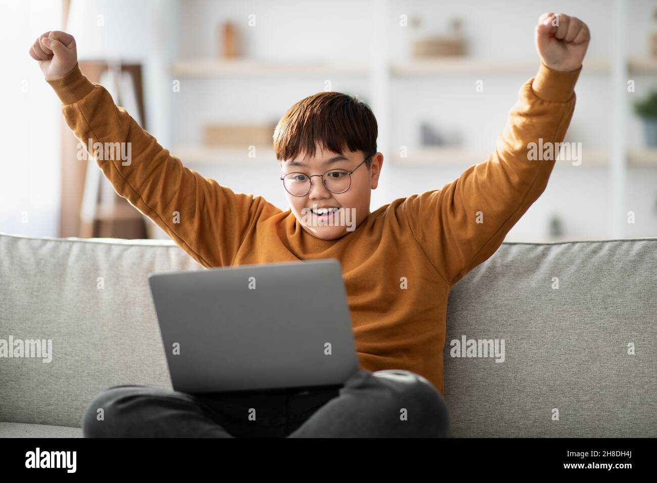 Emotional teenager looking at computer screen and raising hands up Stock Photo