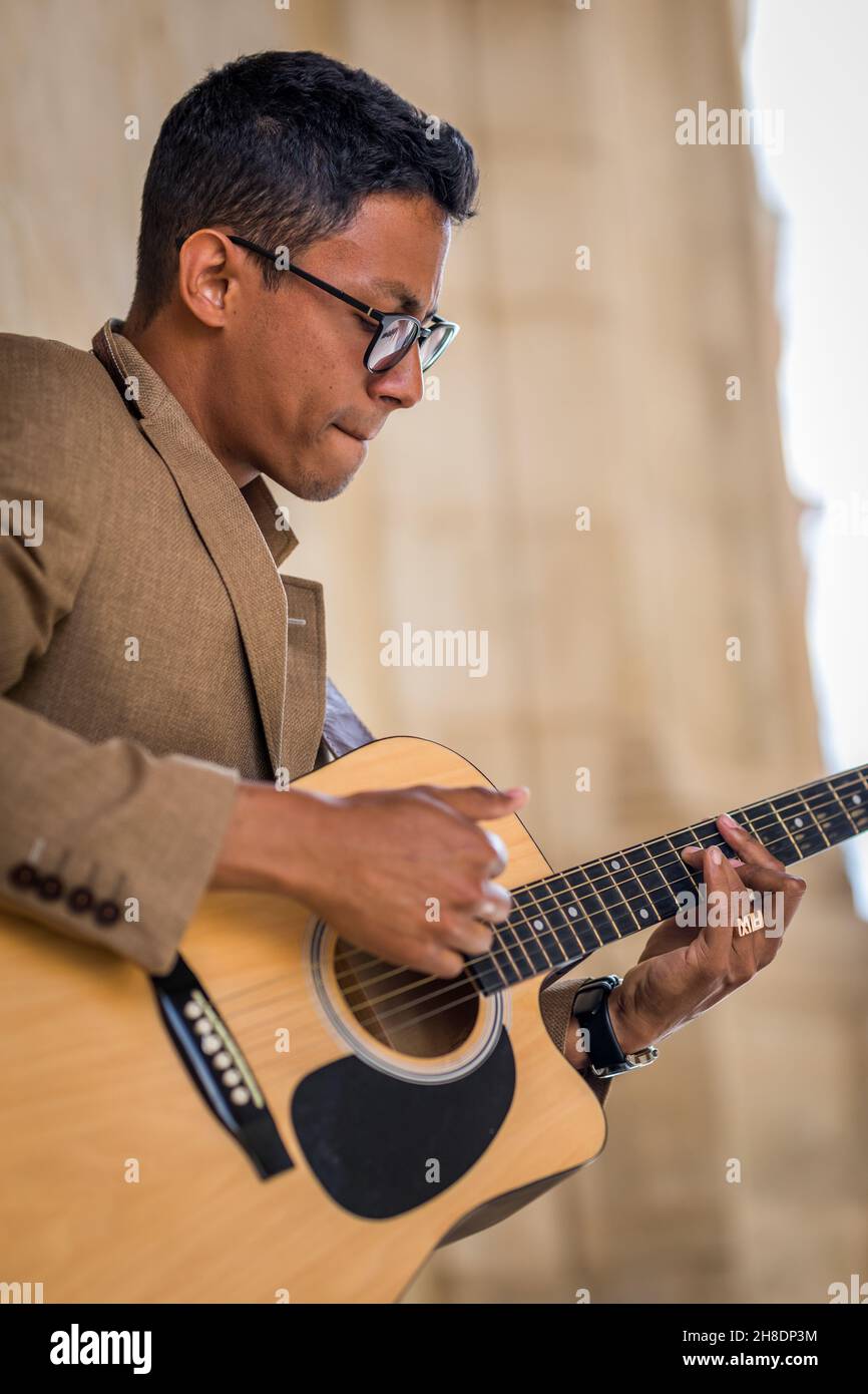 Close up of latin man with glasses playing guitar in the street Stock Photo