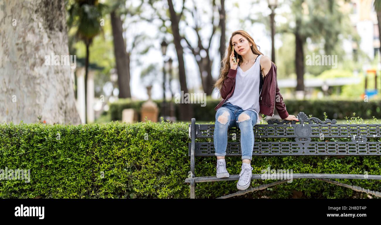 Young girl talking with her smartphone sitting on a bench in the park ...