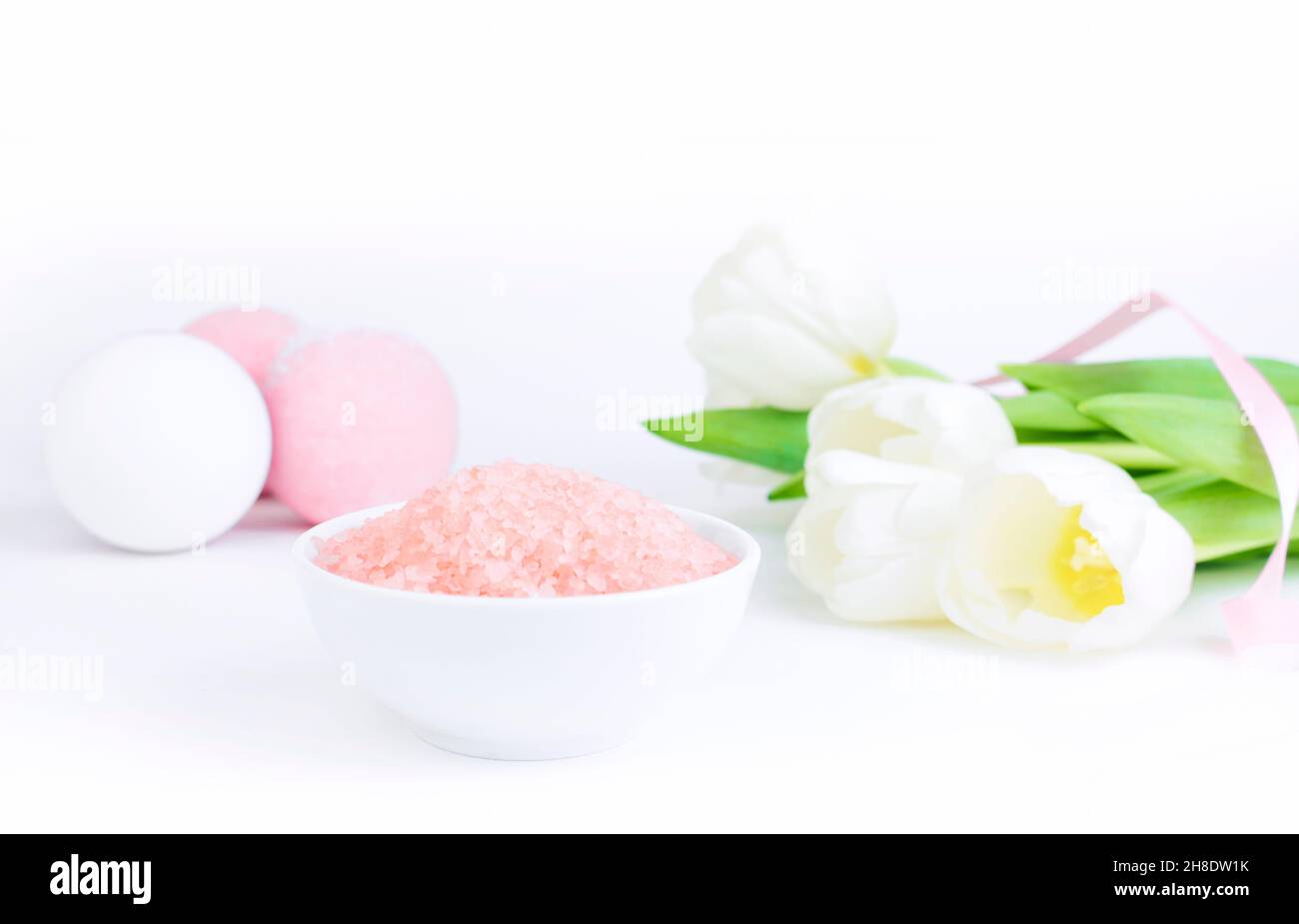 Pink bath salt next to salt bombs and tulips, on a white gray background, are reflected on the mirror surface of the table. The concept of cosmetology Stock Photo