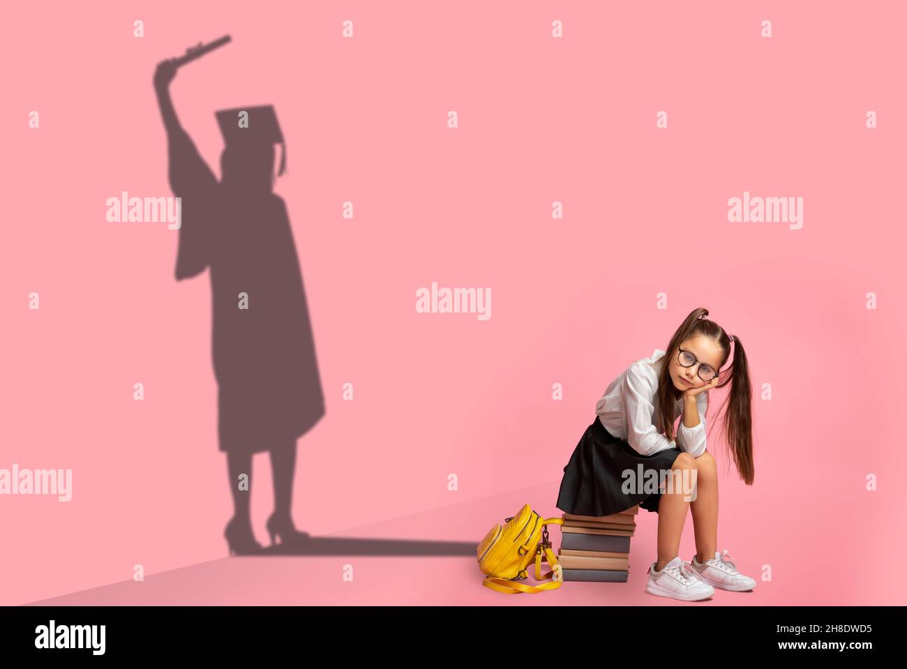 Sad little schoolgirl in glasses dreaming about graduation, conceptual image Stock Photo