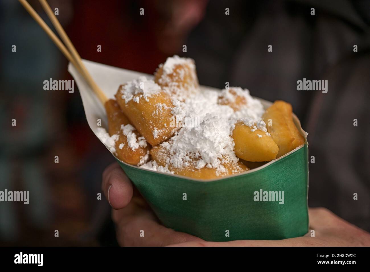 Hand holding a paper bag with mutzenmandeln, deep fried pastry with powdered sugar, typical sweet food for Christmas and new year at a market in Germa Stock Photo