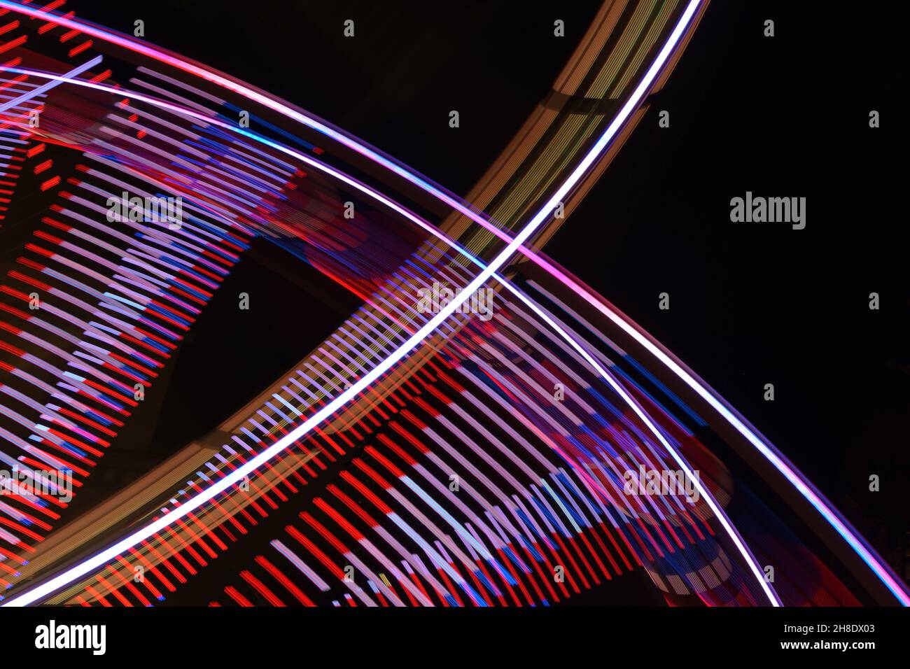 Abstract long exposure of a spinning Ferris wheel and a fast ride on a fun fair at night, colorful light traces in motion blur against a dark sky, cop Stock Photo