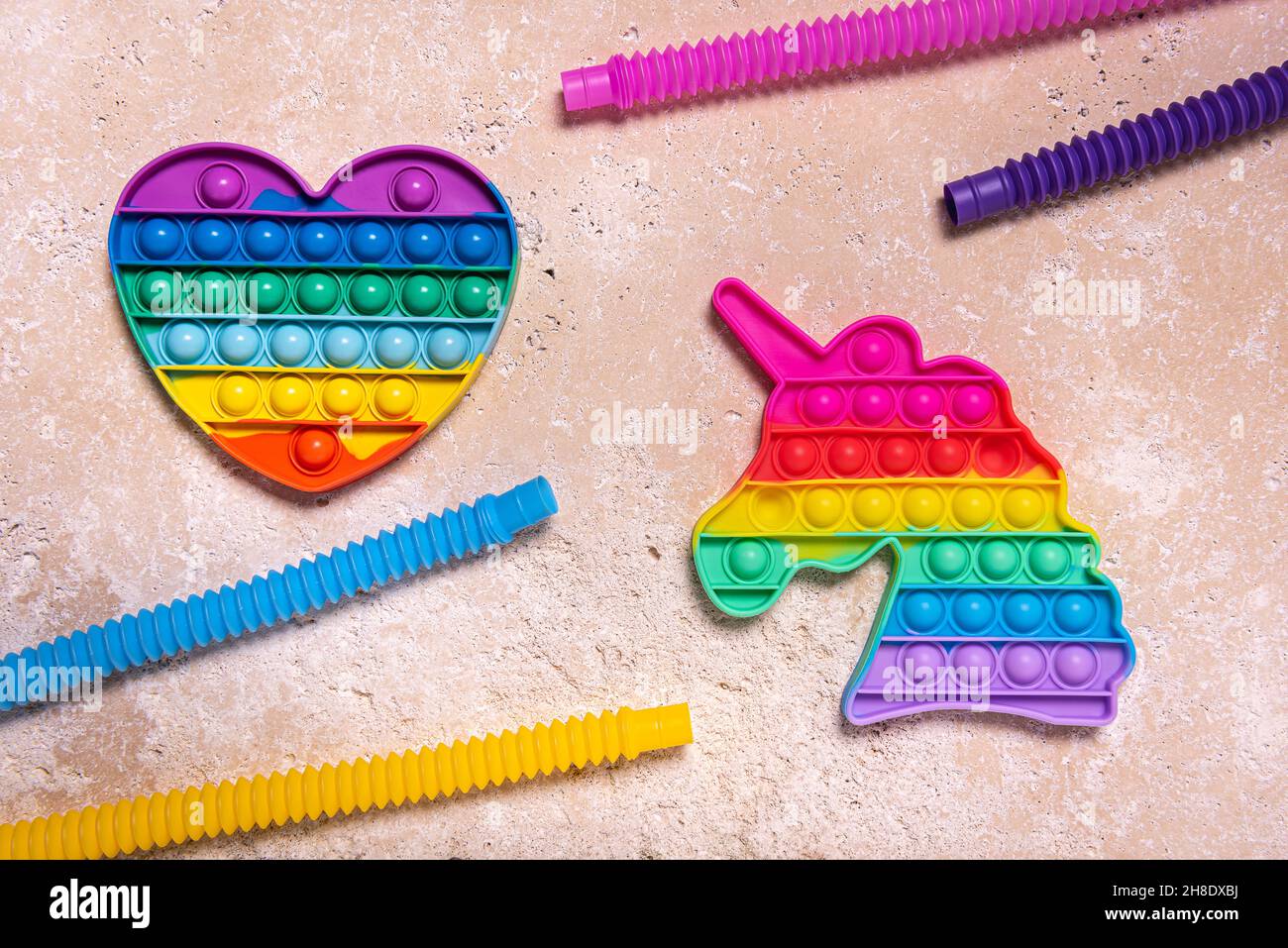 Stretched straight yellow, pink, blue and purple pop it tube children toys, rainbow heart and unicorn. Plastic antistress multicolored toy set on natu Stock Photo