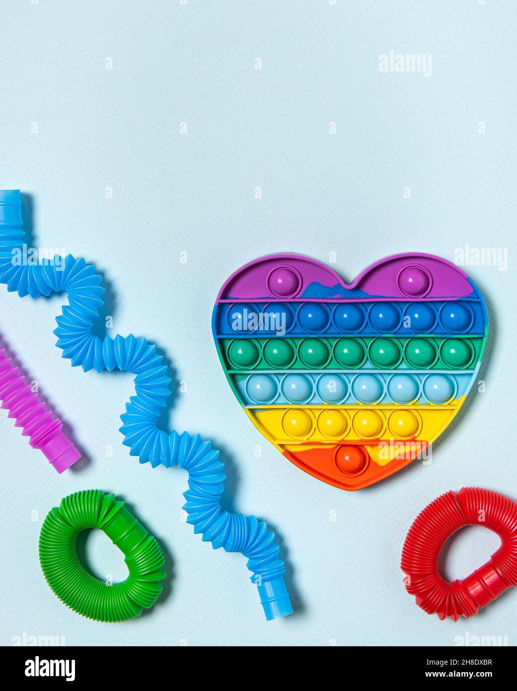 Rainbow heart and red, purple, green, blue and pink pop it tube children toys bent in different shapes. Plastic antistress multicolored toy set on blu Stock Photo