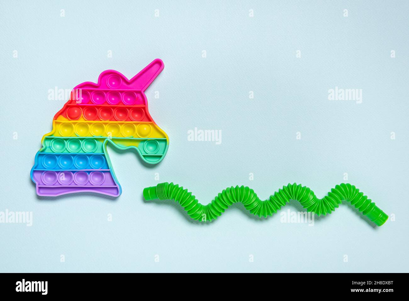 Rainbow unicorn and streched, bent in shape of wave green tube. Pop it children toys in different shapes. Plastic antistress multicolored toy set on b Stock Photo