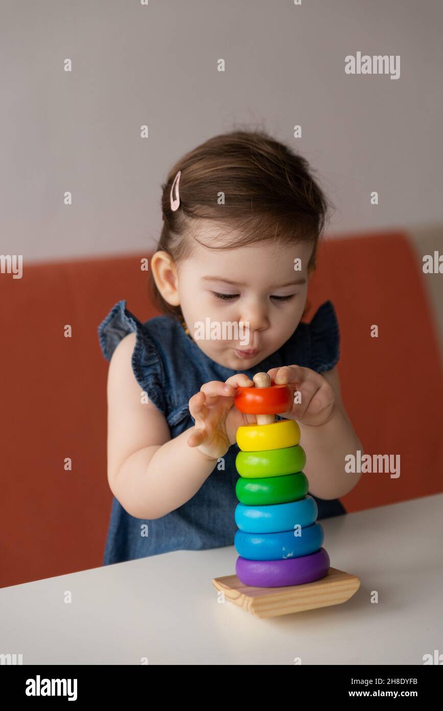 Pretty cute baby girl wearing jeans dress playing colourful toy wooden pyramid and making