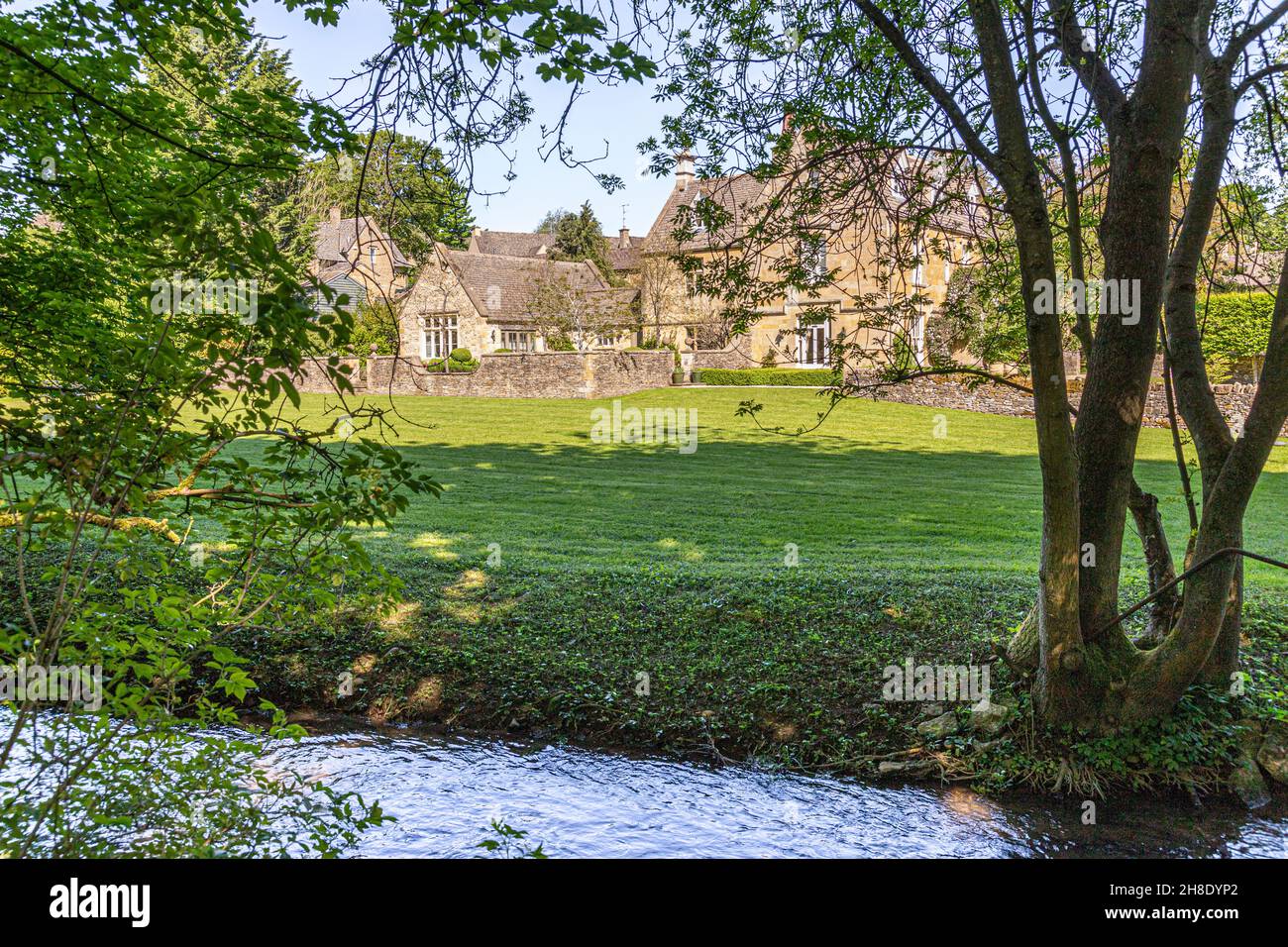 The Manor House beside the infant River Windrush as it flows through the Cotswold village of Naunton, Gloucestershire UK Stock Photo