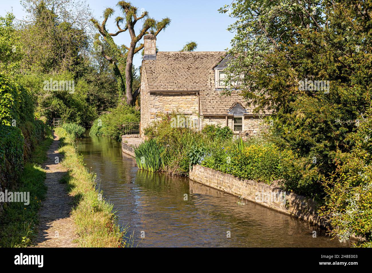 A public footpath opposite a traditional stone cottage beside the infant River Windrush as it flows through the Cotswold village of Naunton, Glouceste Stock Photo
