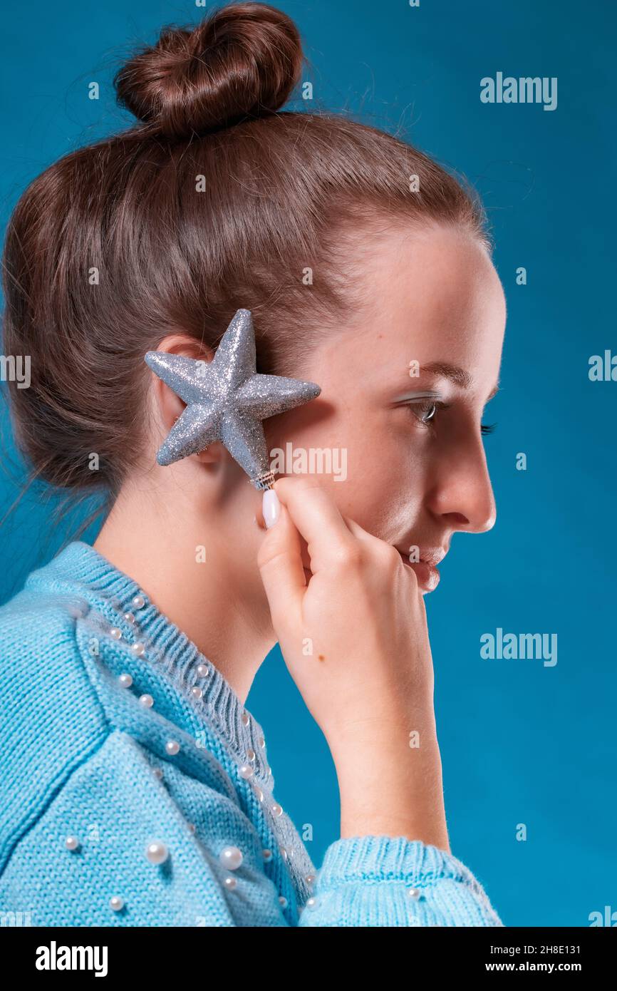 The girl listens to the sounds of the universe, raising a Christmas decoration in the form of a shiny star to her ear. Stock Photo