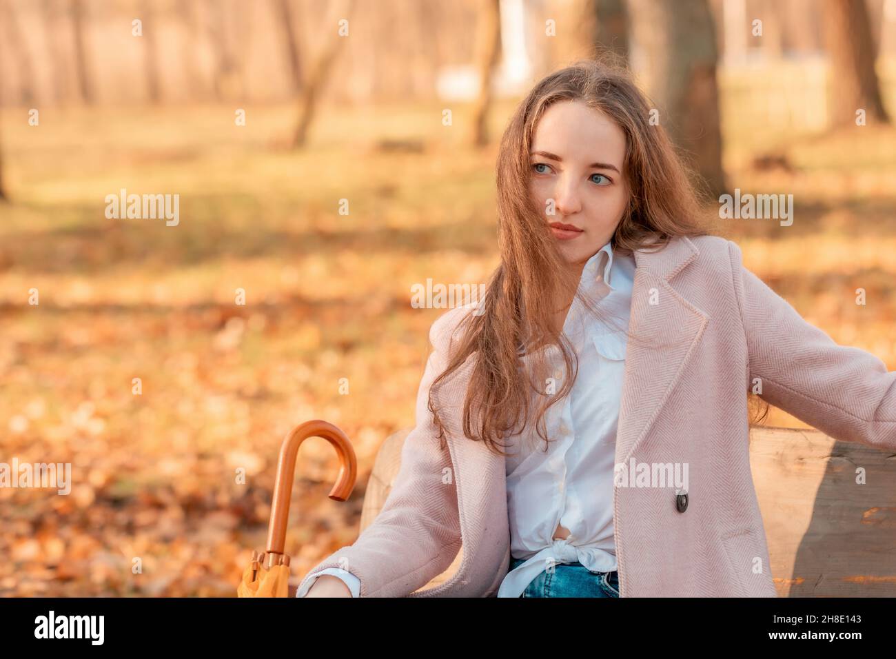 A girl alone sits with an umbrella in her hands on a bench in an autumn park Stock Photo