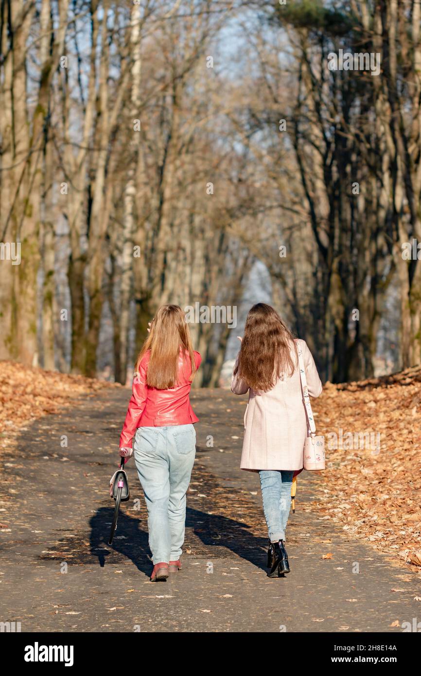 Two young girls are walking in an autumnal October park among trees with fallen leaves Stock Photo