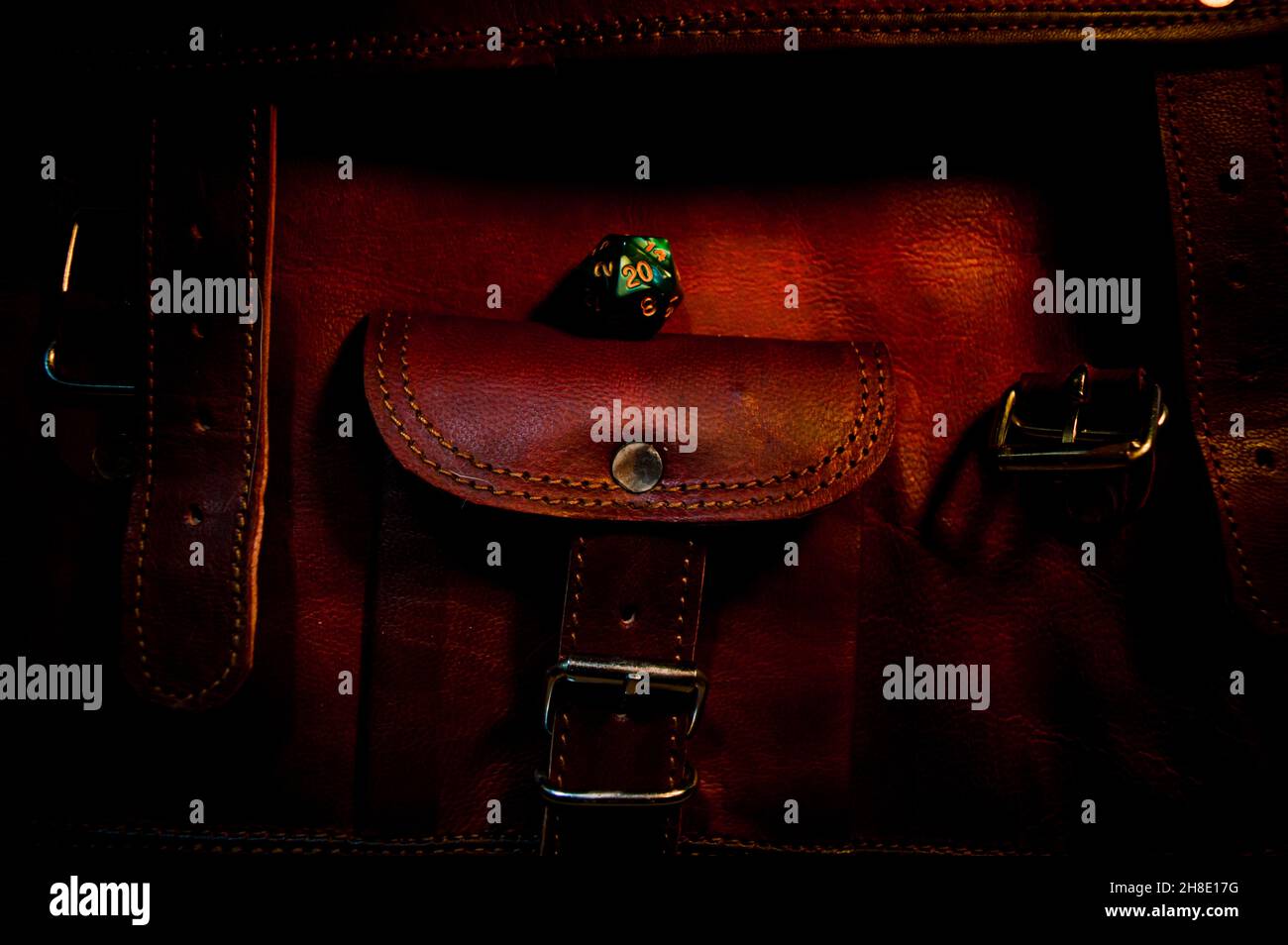 Dark Image of a green 20-sided die on a brown leather bag in warm light Stock Photo