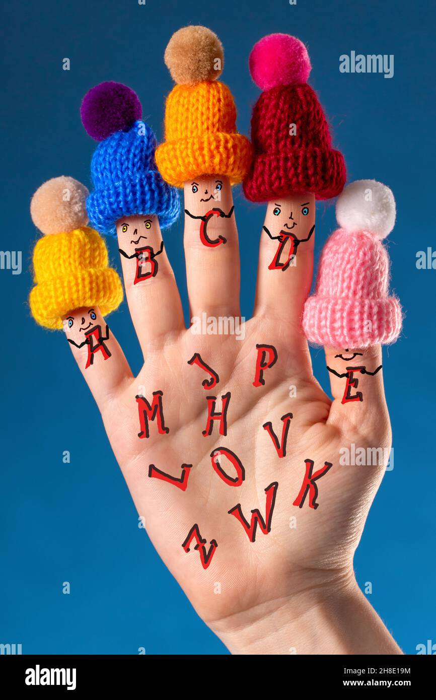 Fingers of the girl's hand with painted smiling faces and dressed hats, like elementary school students, cheerfully collect the alphabet Stock Photo