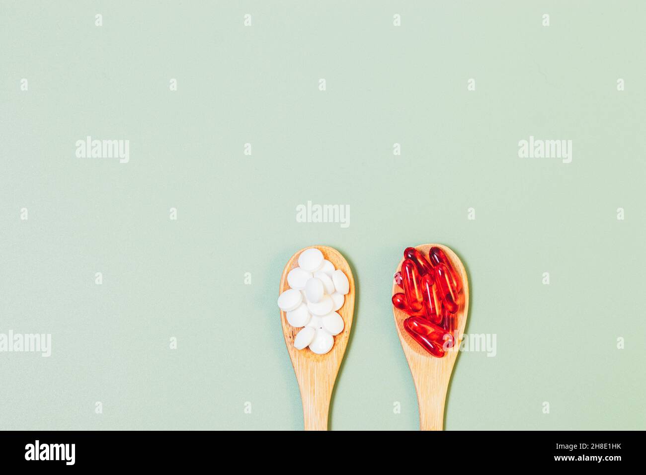 Pills and capsules in wooden spoons on green background with copy space, flat lay Stock Photo