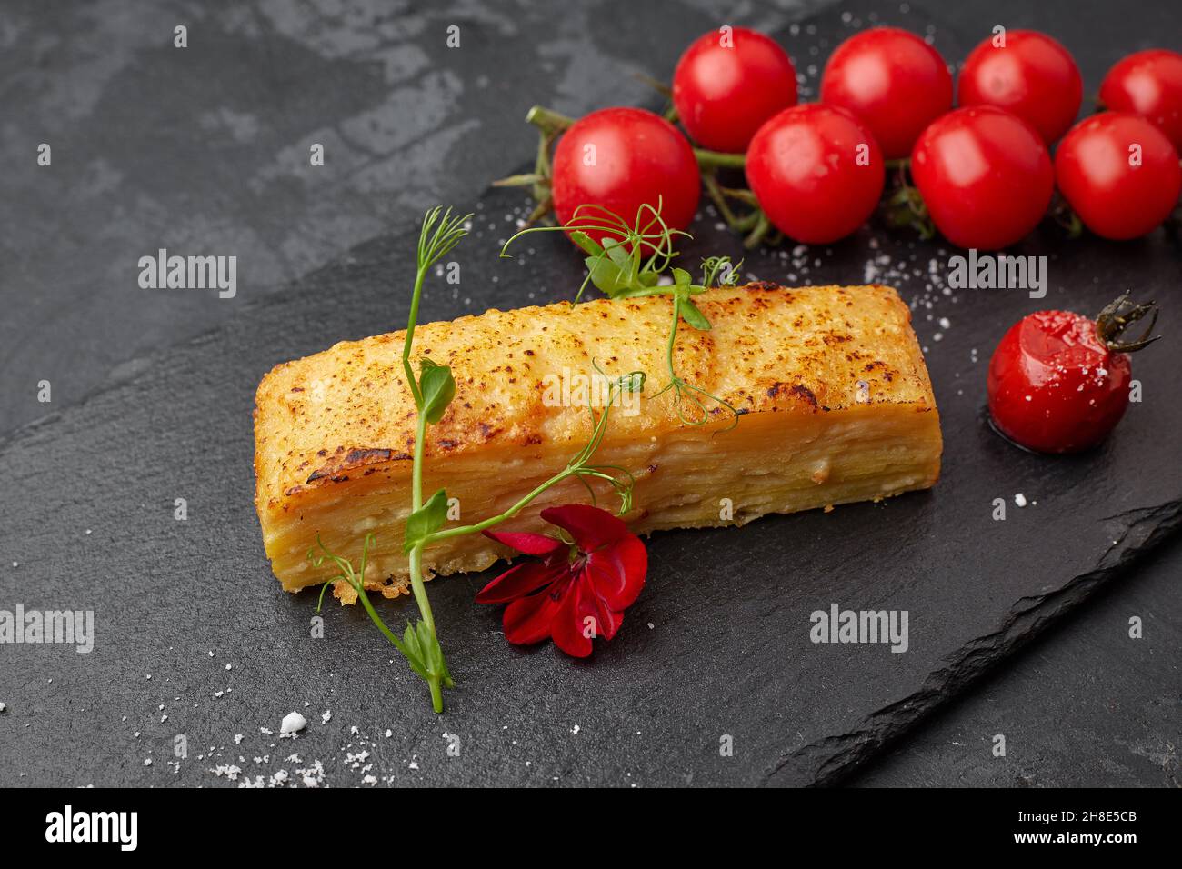 Dauphinua potato gratin with cherry tomatoes on a black stone Stock Photo