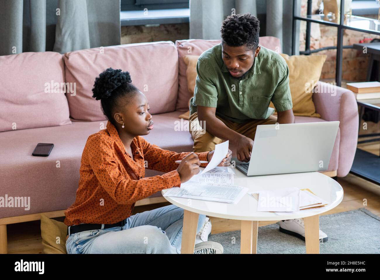 Serious young African American couple sitting at coffee table with papers and laptop and discussing finances Stock Photo
