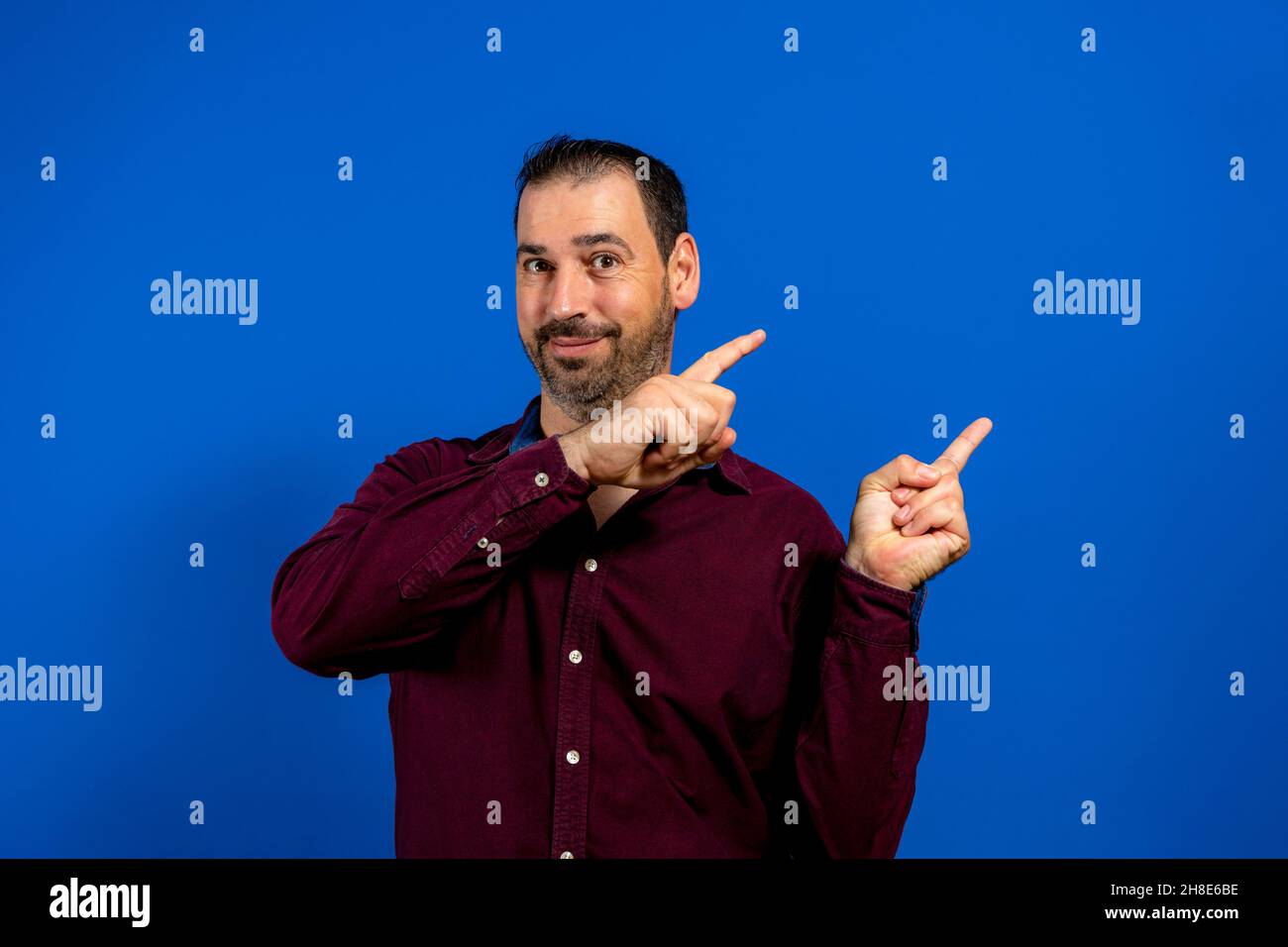 Handsome smiling bearded man pointing away on blue background. Stock Photo