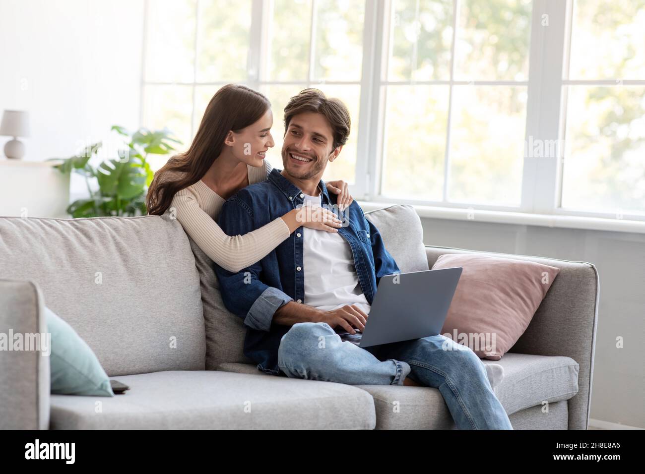 Smiling millennial european lady hugging guy, man work at home, sits on sofa in living room interior Stock Photo