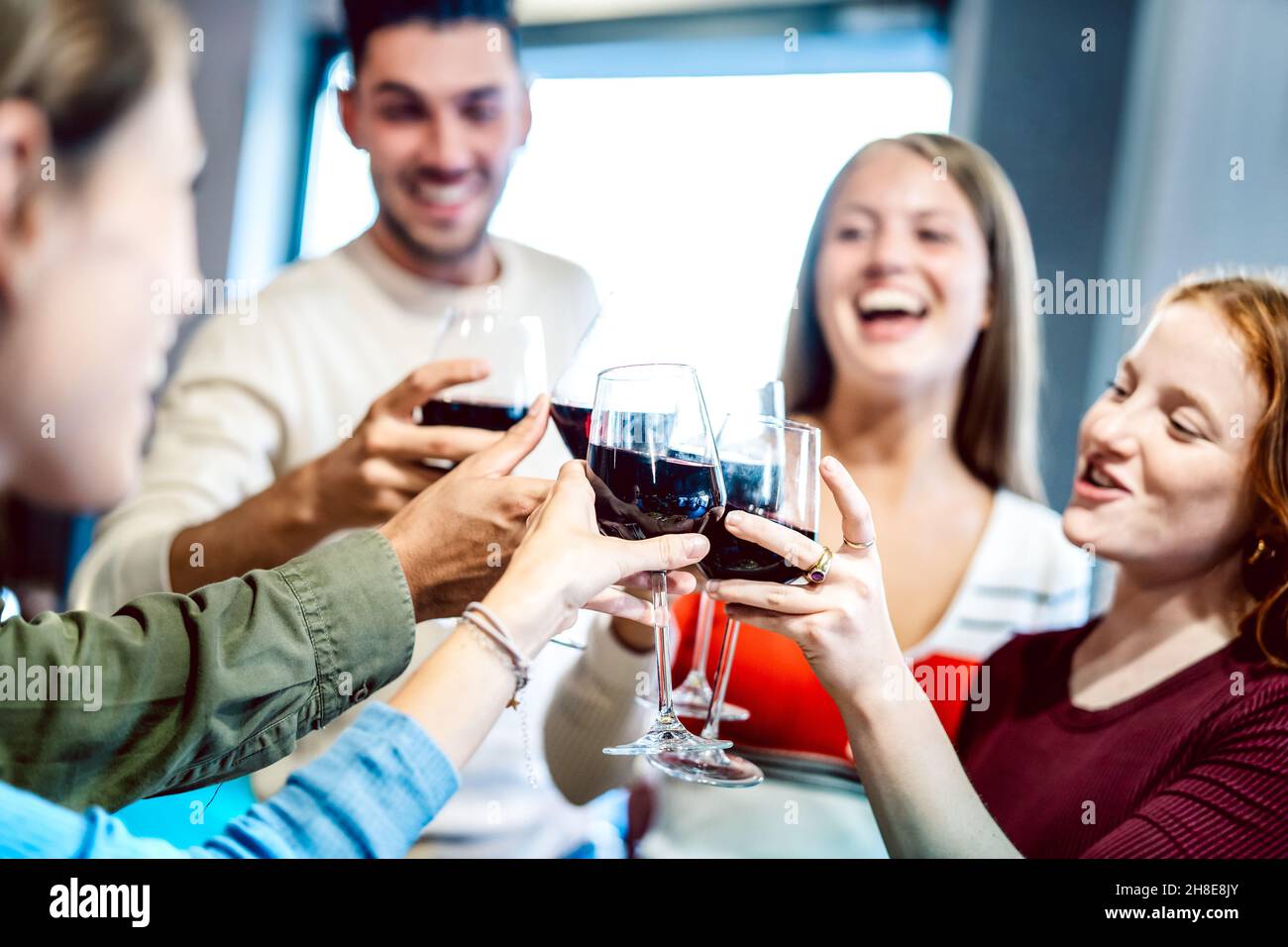 Young multicultural friends drinking and toasting red wine at  home party - Happy people having fun together at restaurant winery bar Stock Photo